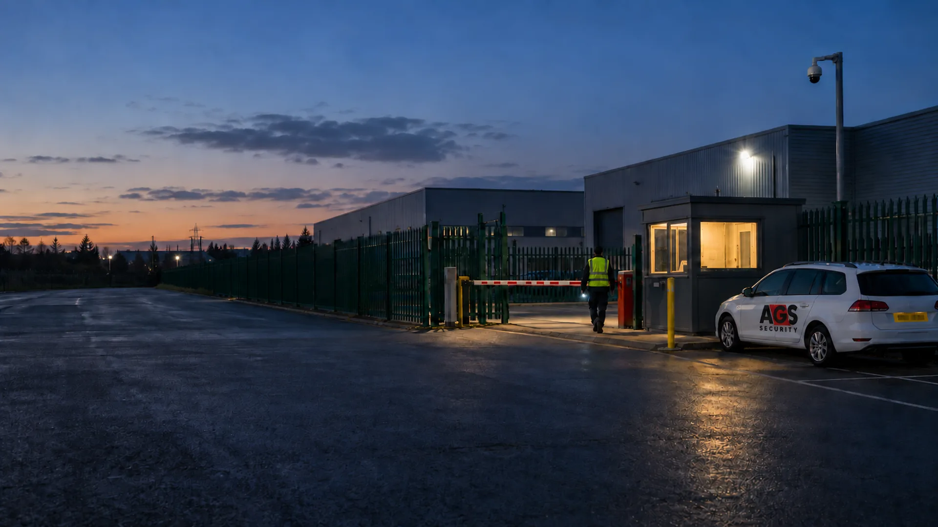 Security officer, gatehouse and marked AGS patrol vehicle at the entrance of a commercial industrial site at dusk