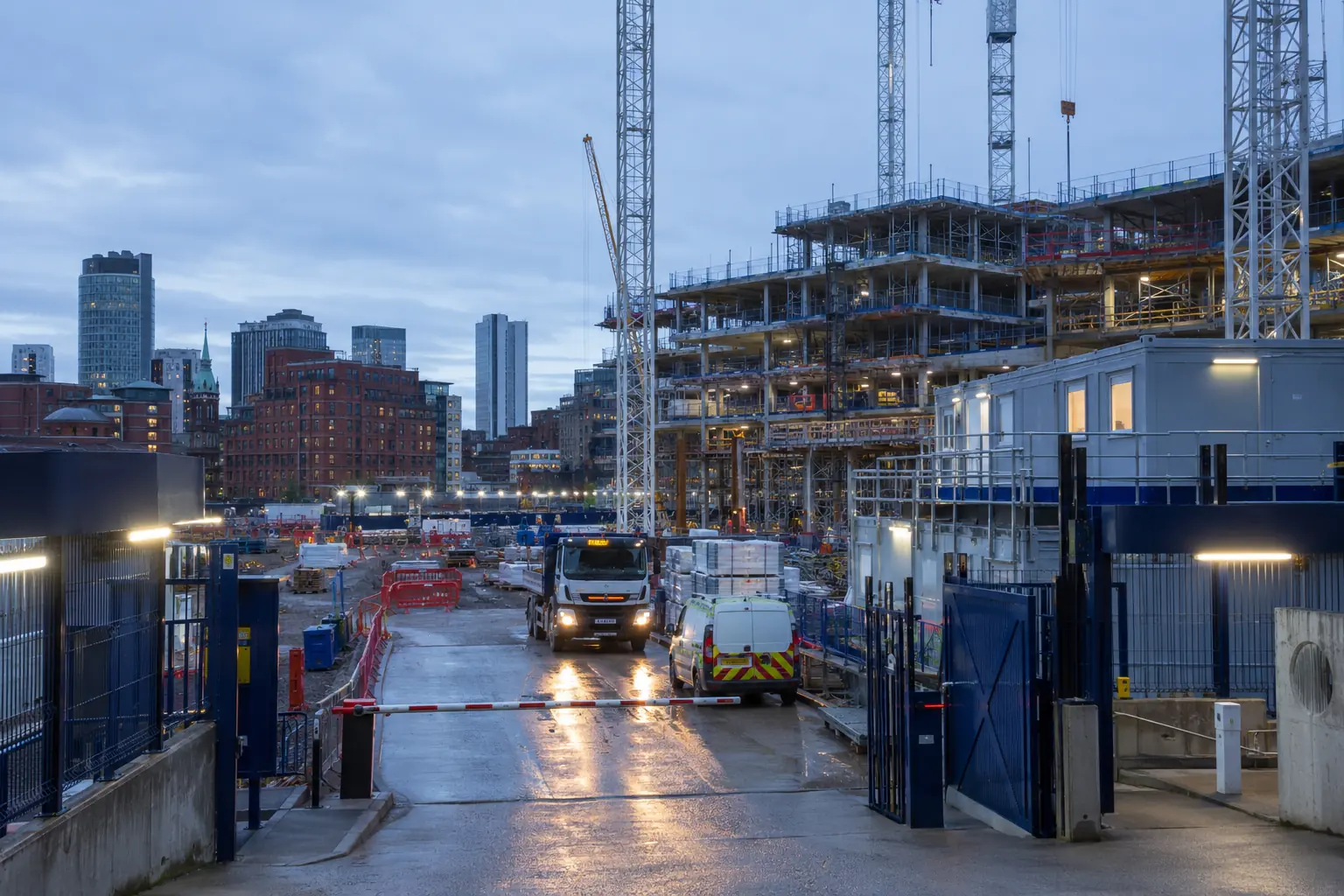 Controlled entrance to a large urban construction site with cranes and secure perimeter fencing
