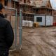 AGS Security officer viewed from behind at the open gate of a part-built housing development, with heras fencing, scaffolding and a site cabin