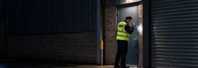 Security officer checking the door of a commercial unit with a torch during a night alarm response