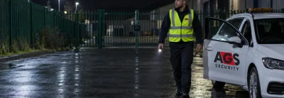 Security officer on a night mobile patrol beside a marked AGS patrol vehicle at an industrial estate